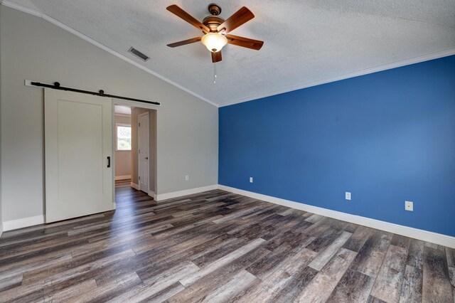 unfurnished bedroom with wood finished floors, a barn door, vaulted ceiling, visible vents, and a textured ceiling