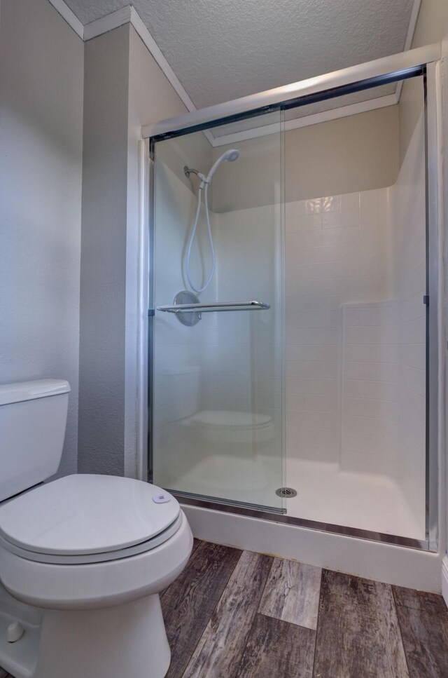 bathroom with wood finished floors, a shower stall, a textured ceiling, and toilet