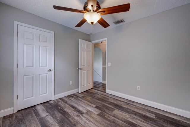unfurnished bedroom with a textured ceiling, visible vents, ceiling fan, dark wood-style floors, and baseboards