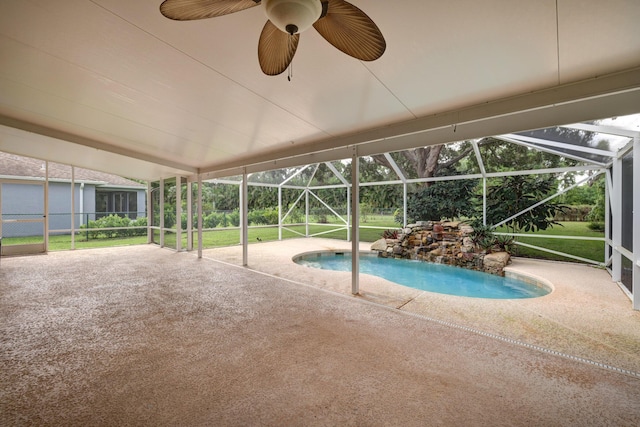 pool with a lawn, a patio, ceiling fan, and glass enclosure