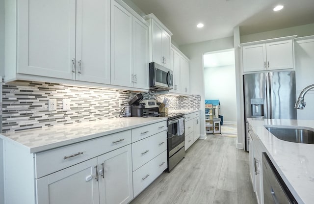 15581 Goldfinch Cir, The Acreage, FL 33470 - kitchen featuring appliances with stainless steel finishes, a sink, light stone countertops, decorative backsplash, and light wood-type flooring