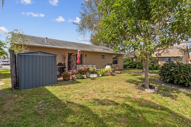back of property featuring stucco siding, an outdoor structure, a lawn, and a patio