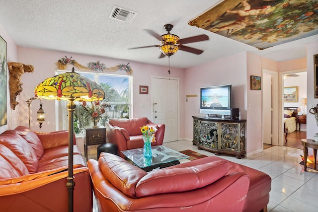 living room featuring light tile patterned flooring, visible vents, a ceiling fan, and a textured ceiling