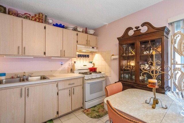 kitchen featuring a textured ceiling, a sink, light countertops, white range with gas cooktop, and under cabinet range hood