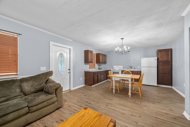 living area with light wood finished floors, a textured ceiling, baseboards, an inviting chandelier, and crown molding