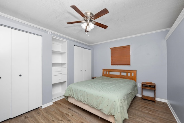 bedroom featuring baseboards, multiple closets, wood finished floors, and ornamental molding