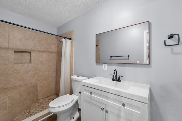 full bathroom with a tile shower, a textured ceiling, toilet, and vanity