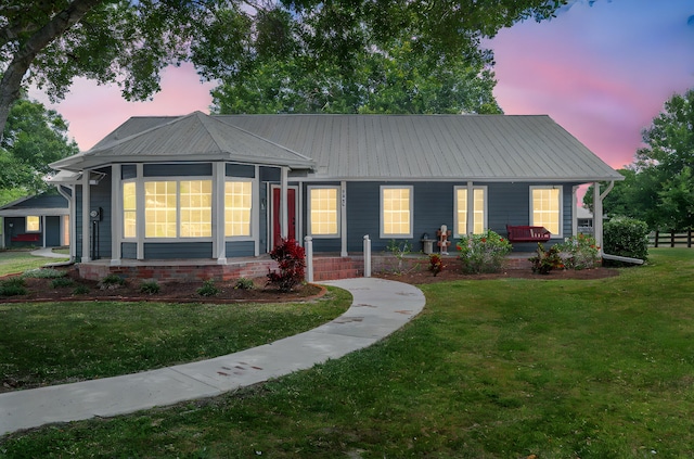 ranch-style home featuring metal roof, covered porch, and a front yard