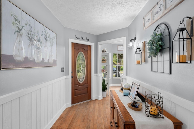 foyer with a textured ceiling, light wood finished floors, and wainscoting