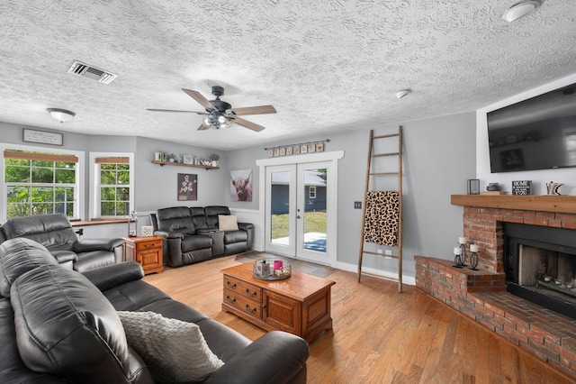 living area featuring a textured ceiling, visible vents, light wood-style floors, a ceiling fan, and a fireplace