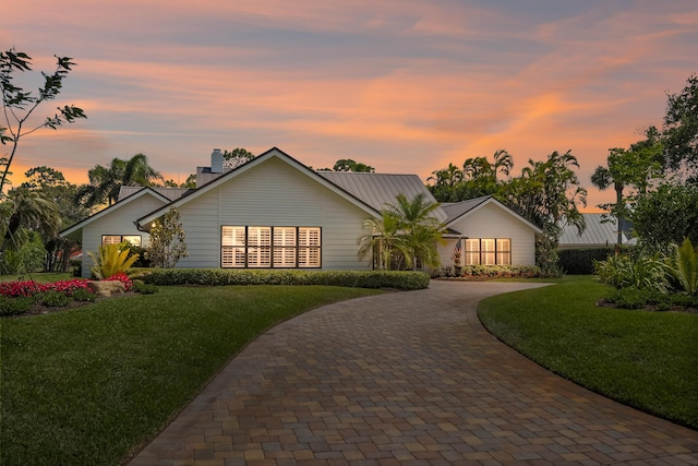 ranch-style house with a chimney, curved driveway, and a lawn
