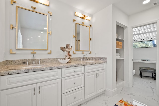 bathroom featuring a sink, toilet, marble finish floor, double vanity, and visible vents