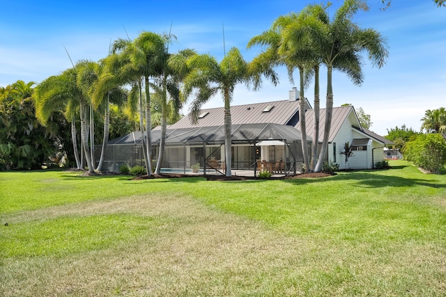back of house featuring a chimney, glass enclosure, and a yard