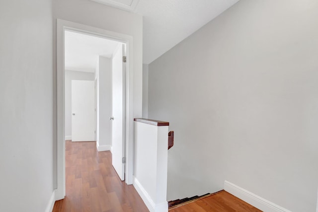 corridor featuring an upstairs landing, wood finished floors, and baseboards