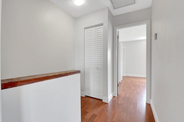 hallway with baseboards, visible vents, a textured ceiling, and light wood finished floors