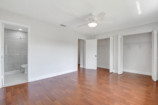 unfurnished bedroom featuring wood finished floors, visible vents, multiple closets, and connected bathroom