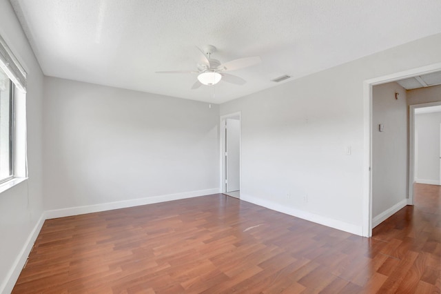 spare room featuring visible vents, baseboards, attic access, wood finished floors, and a ceiling fan