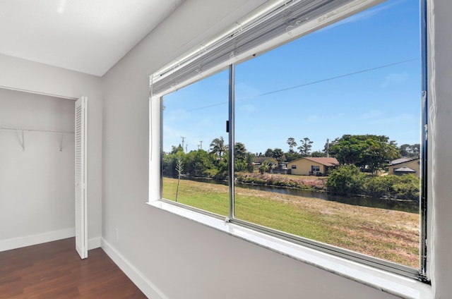 unfurnished bedroom featuring dark wood finished floors, baseboards, a water view, and a closet