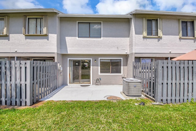 rear view of house featuring stucco siding, fence, central air condition unit, a patio, and a lawn