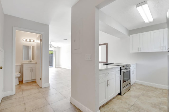 kitchen featuring light tile patterned floors, white cabinetry, stainless steel range with electric cooktop, and light countertops