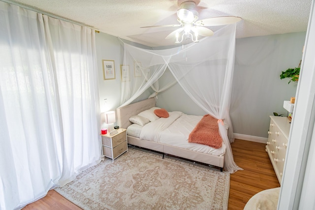 bedroom featuring baseboards, wood finished floors, a ceiling fan, and a textured ceiling