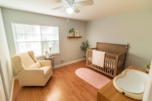 bedroom with light wood-style floors, ceiling fan, a nursery area, and baseboards
