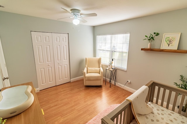 bedroom featuring a closet, ceiling fan, a nursery area, baseboards, and wood finished floors