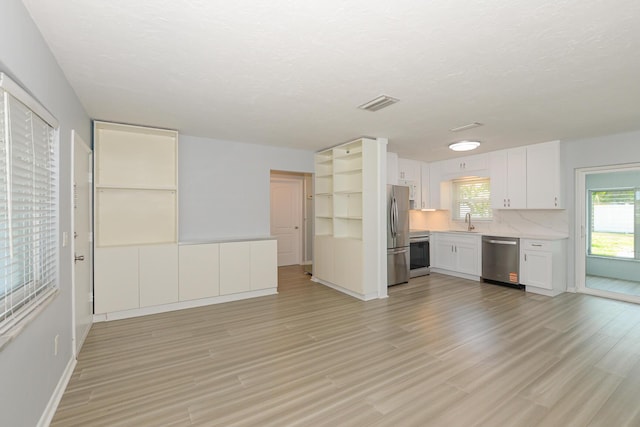 712 NE Camino St, Port Saint Lucie, FL 34952 - unfurnished living room with a sink, light wood-style floors, a textured ceiling, baseboards, and visible vents