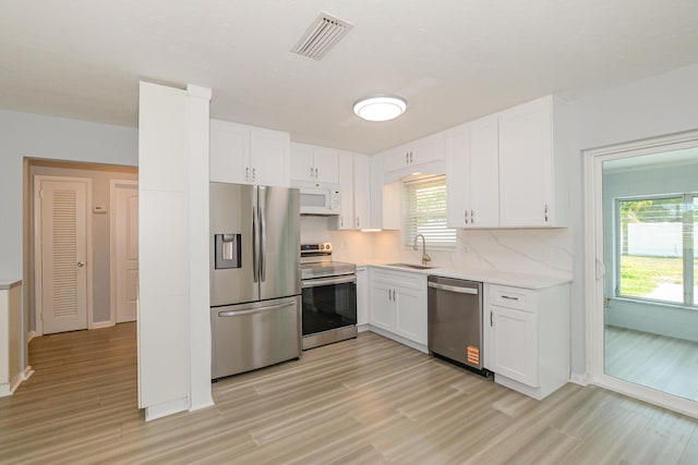 712 NE Camino St, Port Saint Lucie, FL 34952 - kitchen with visible vents, a sink, light wood finished floors, stainless steel appliances, and white cabinetry