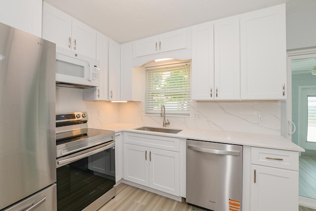 712 NE Camino St, Port Saint Lucie, FL 34952 - kitchen with decorative backsplash, white cabinetry, a sink, light wood-style flooring, and appliances with stainless steel finishes