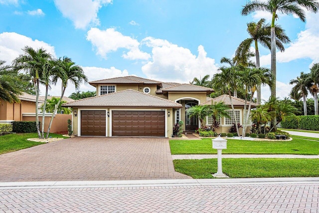 mediterranean / spanish house featuring a tiled roof, decorative driveway, an attached garage, stucco siding, and a front lawn