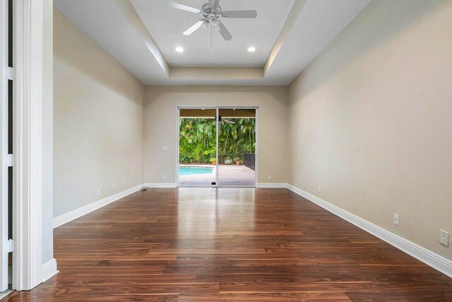 empty room with recessed lighting, a raised ceiling, a ceiling fan, baseboards, and wood finished floors