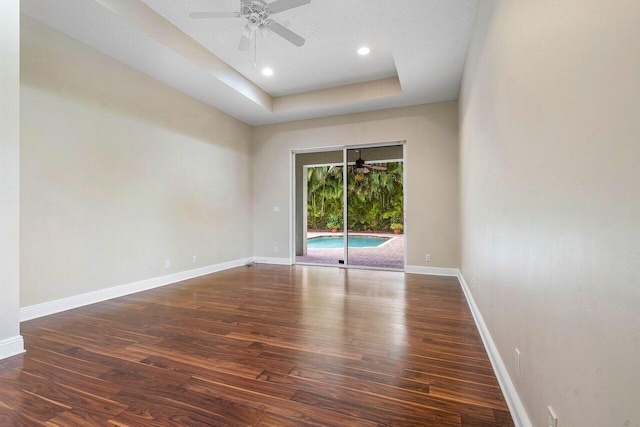 unfurnished room featuring a tray ceiling, ceiling fan, wood finished floors, and baseboards