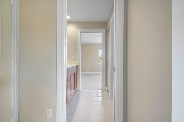 hall featuring light tile patterned floors, light carpet, and baseboards
