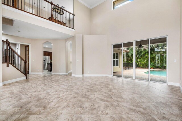 6616 Cobia Cir, Boynton Beach, FL 33437 - unfurnished living room with a towering ceiling, arched walkways, a ceiling fan, baseboards, and stairs