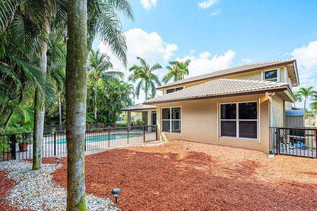 rear view of property with stucco siding, fence, and a tile roof
