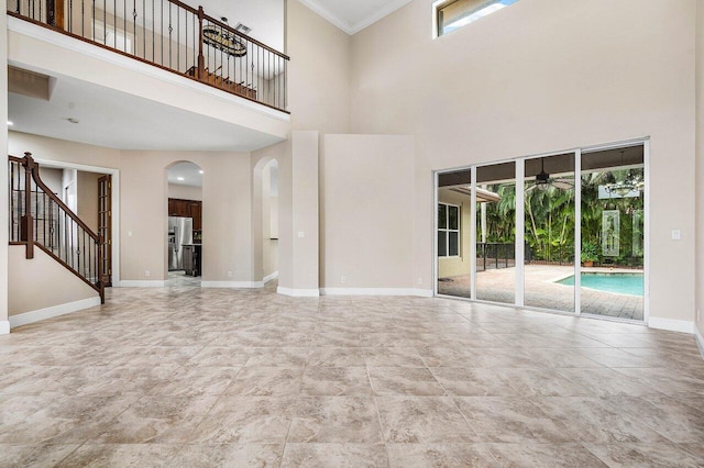 unfurnished living room with arched walkways, stairs, ceiling fan, baseboards, and a high ceiling