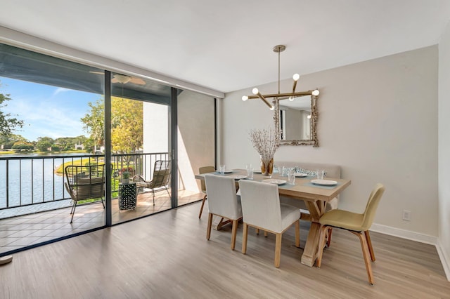 dining space featuring wood finished floors, a water view, a wall of windows, baseboards, and a notable chandelier