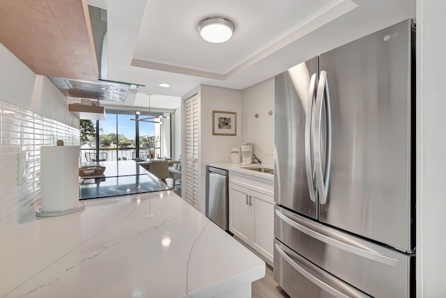 kitchen with light stone counters, white cabinets, a raised ceiling, stainless steel appliances, and island exhaust hood
