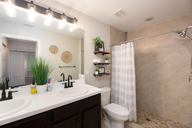 bathroom with visible vents, toilet, a tile shower, and a sink