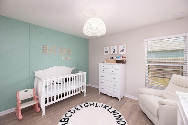 bedroom featuring a crib, a notable chandelier, wood finished floors, and baseboards