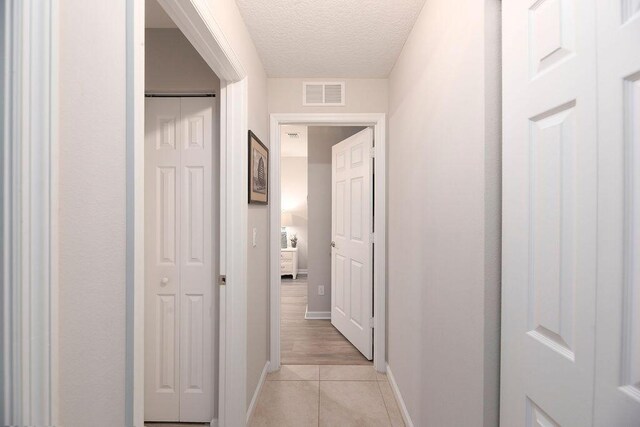 hall featuring baseboards, visible vents, a textured ceiling, and light tile patterned flooring