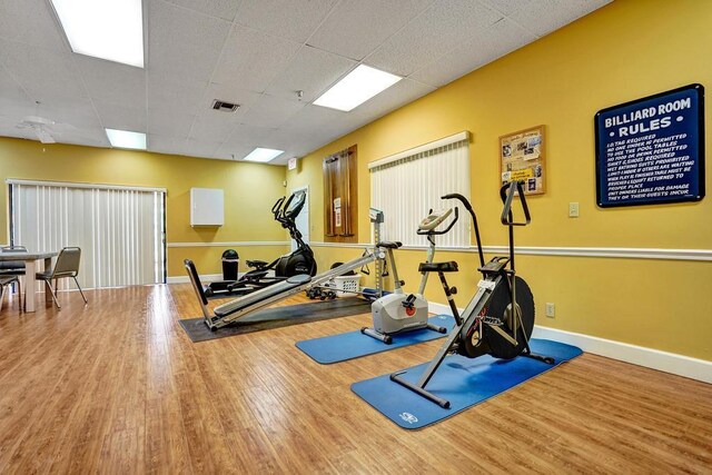 exercise area featuring visible vents, baseboards, wood finished floors, and a paneled ceiling