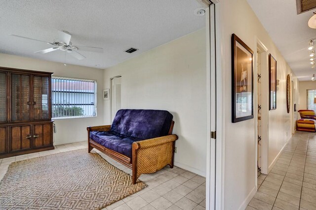 living area featuring ceiling fan, a textured ceiling, visible vents, baseboards, and light tile patterned flooring