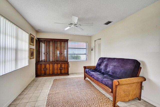 living area featuring a textured ceiling, a ceiling fan, baseboards, light tile patterned floors, and visible vents