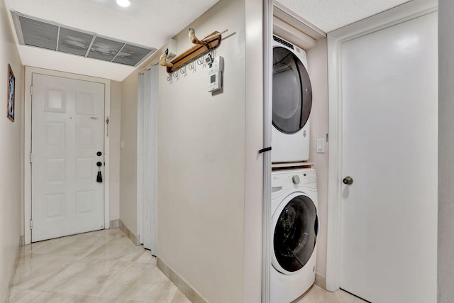 clothes washing area with visible vents, stacked washer / dryer, laundry area, and baseboards
