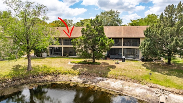 rear view of property featuring a lawn, a water view, and a shingled roof