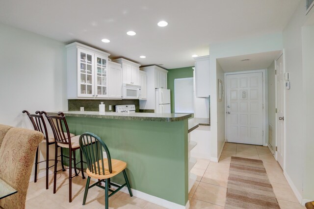 kitchen with dark countertops, tasteful backsplash, light tile patterned floors, white appliances, and white cabinetry