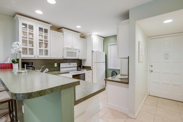 kitchen featuring a sink, dark countertops, a peninsula, and white appliances