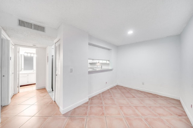 tiled empty room featuring a textured ceiling, visible vents, recessed lighting, and baseboards